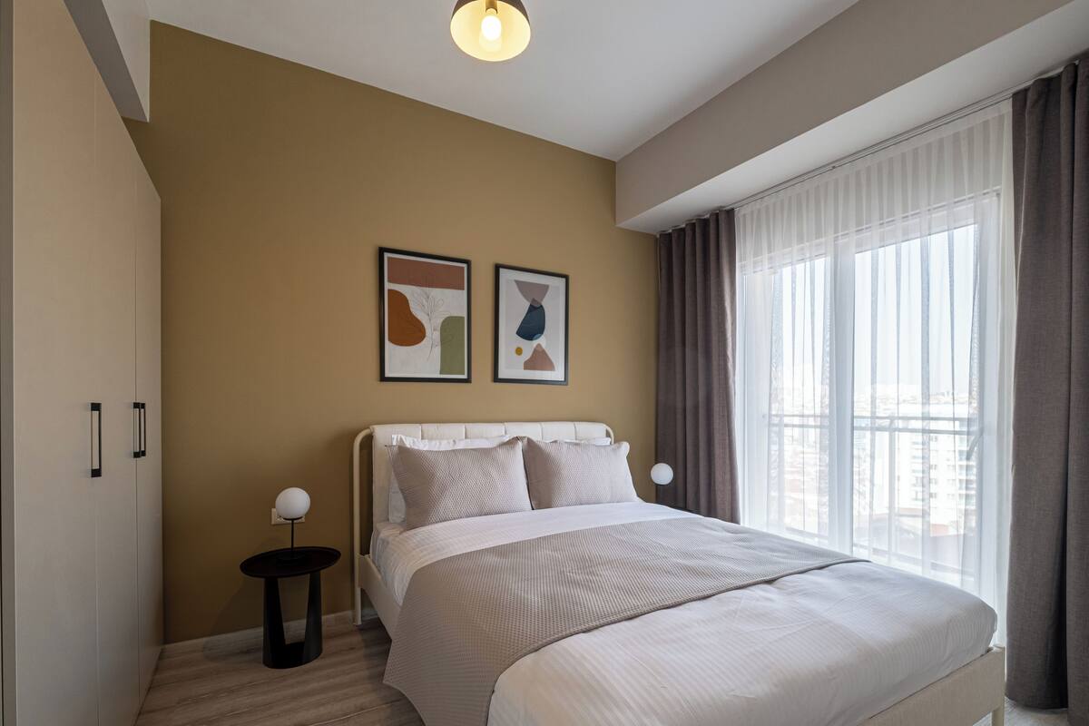 A modern hotel room with a large bed, a nightstand, and a window with curtains.