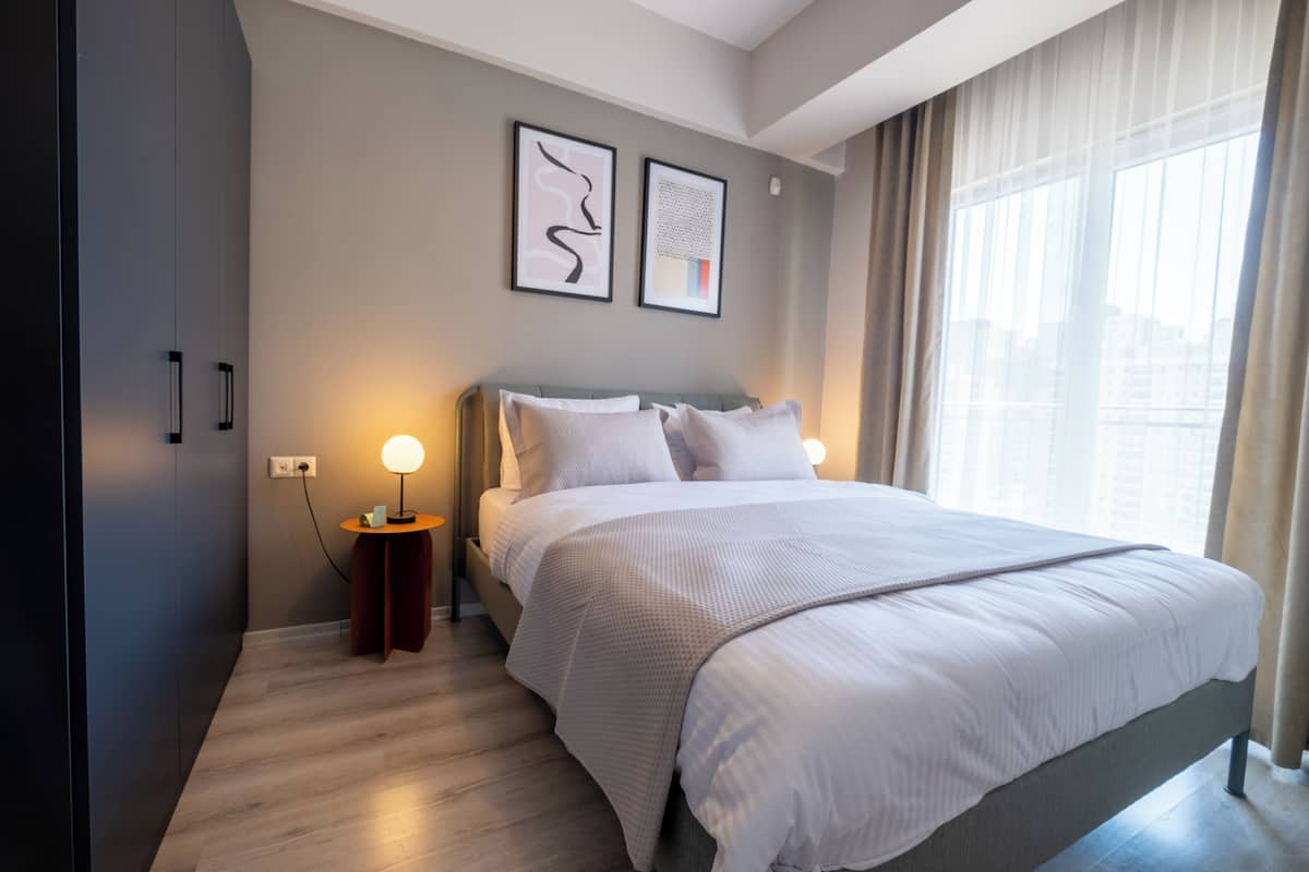 A modern bedroom with a large bed, a bedside table with a lamp, and two framed artworks on the wall.