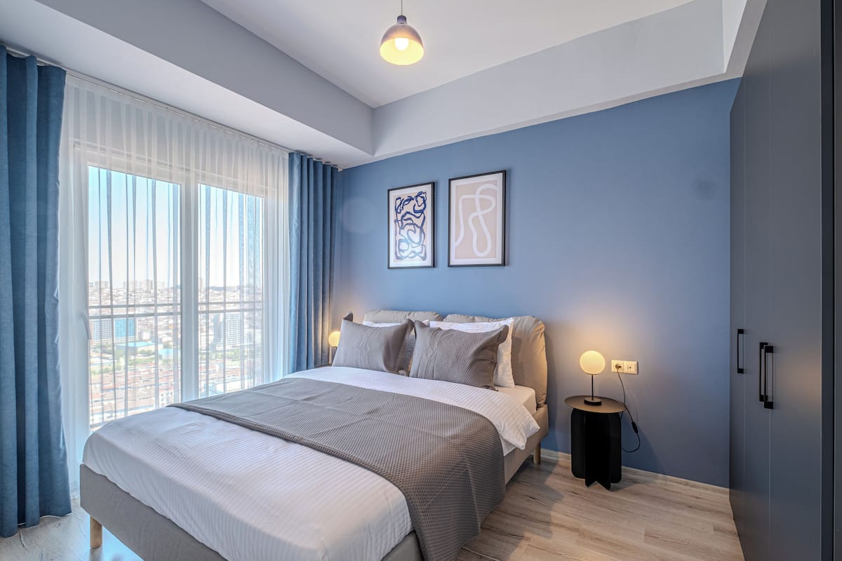 A modern bedroom with a large bed, a bedside table with a lamp, and two framed artworks on the wall.