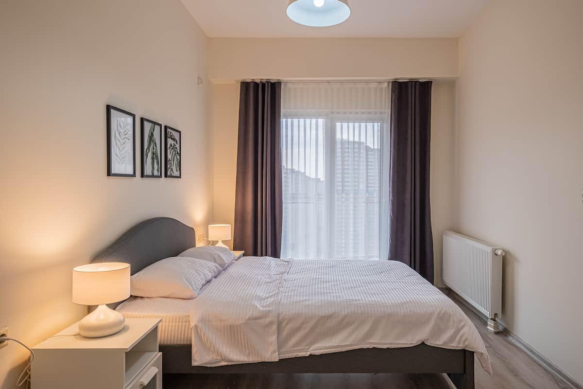 A neatly arranged bedroom with a bed, bedside tables, and a window with curtains.