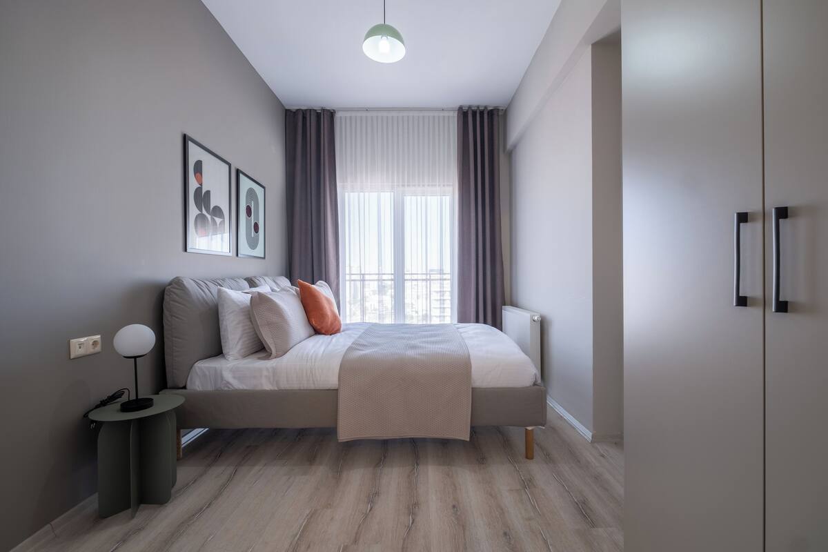 A modern bedroom with a bed, bedside table, and a window with curtains.