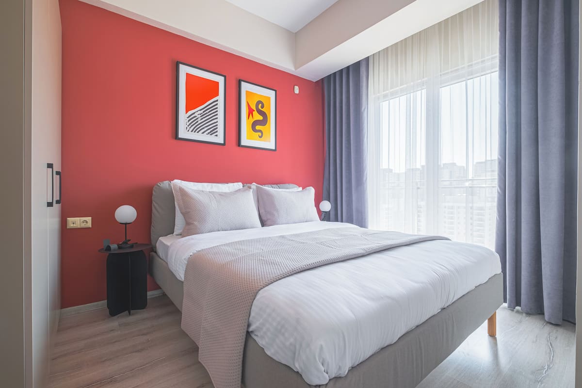 A modern bedroom with a large bed, red walls, and two framed artworks.