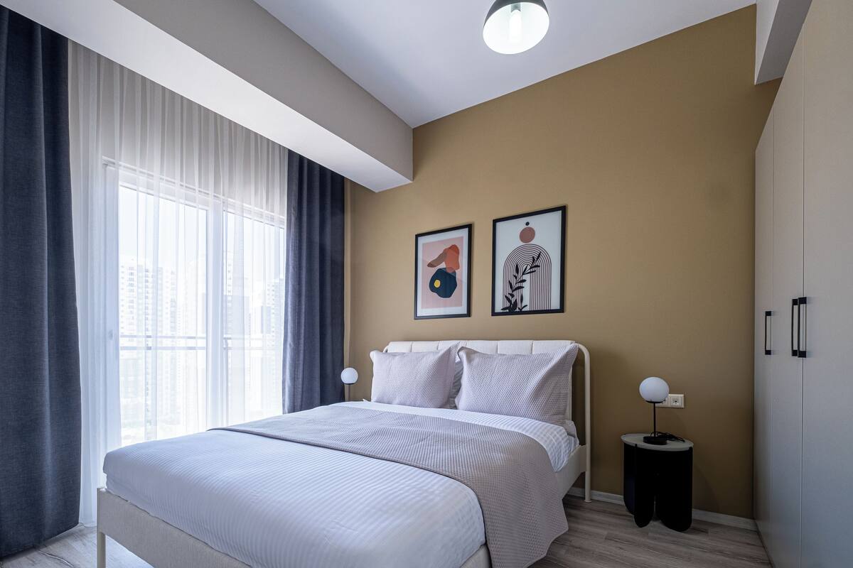 A modern bedroom with a large bed, a bedside table with a lamp, and two framed artworks on the wall.