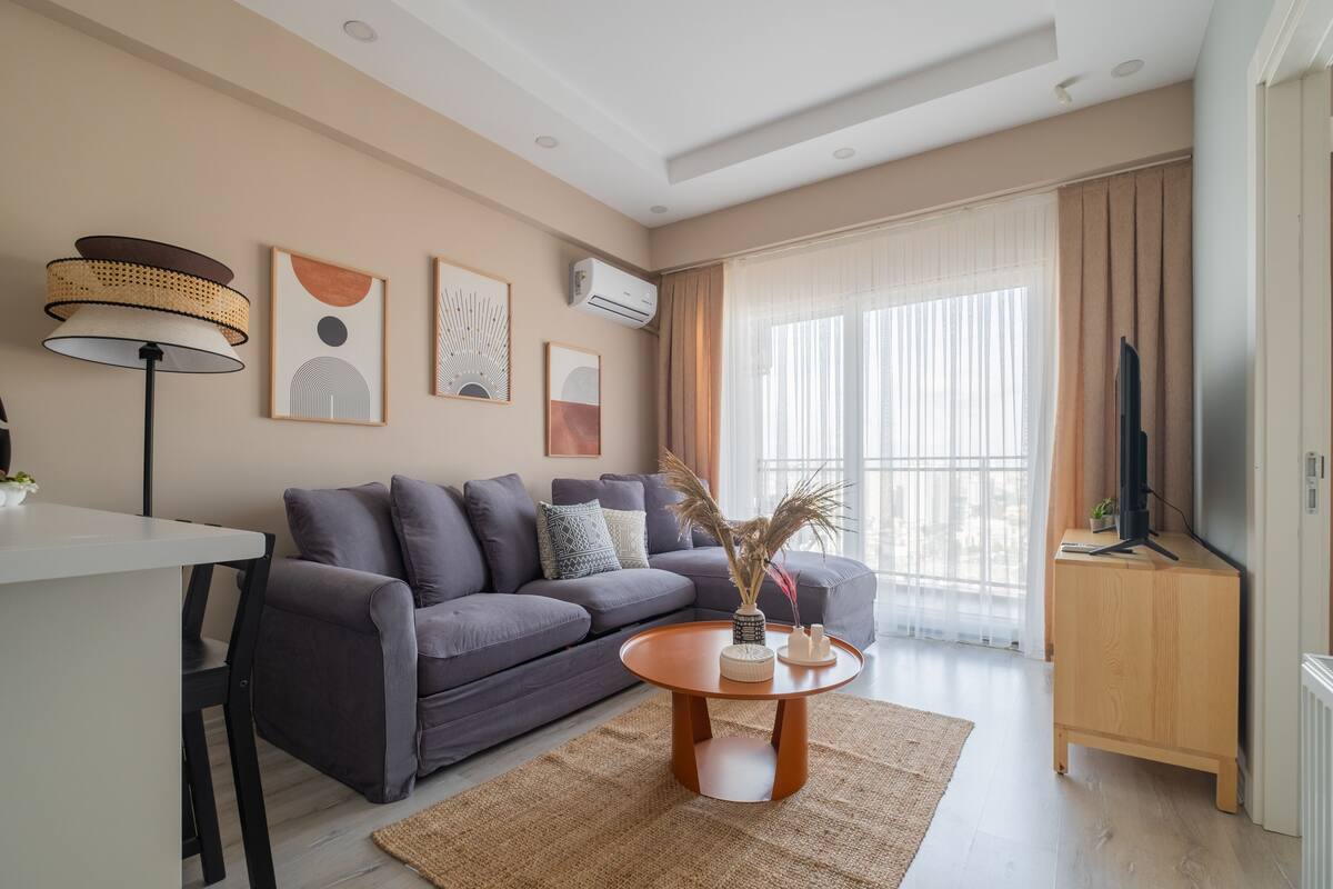A modern living room with a grey sofa, a round wooden coffee table, and a TV on a wooden stand.