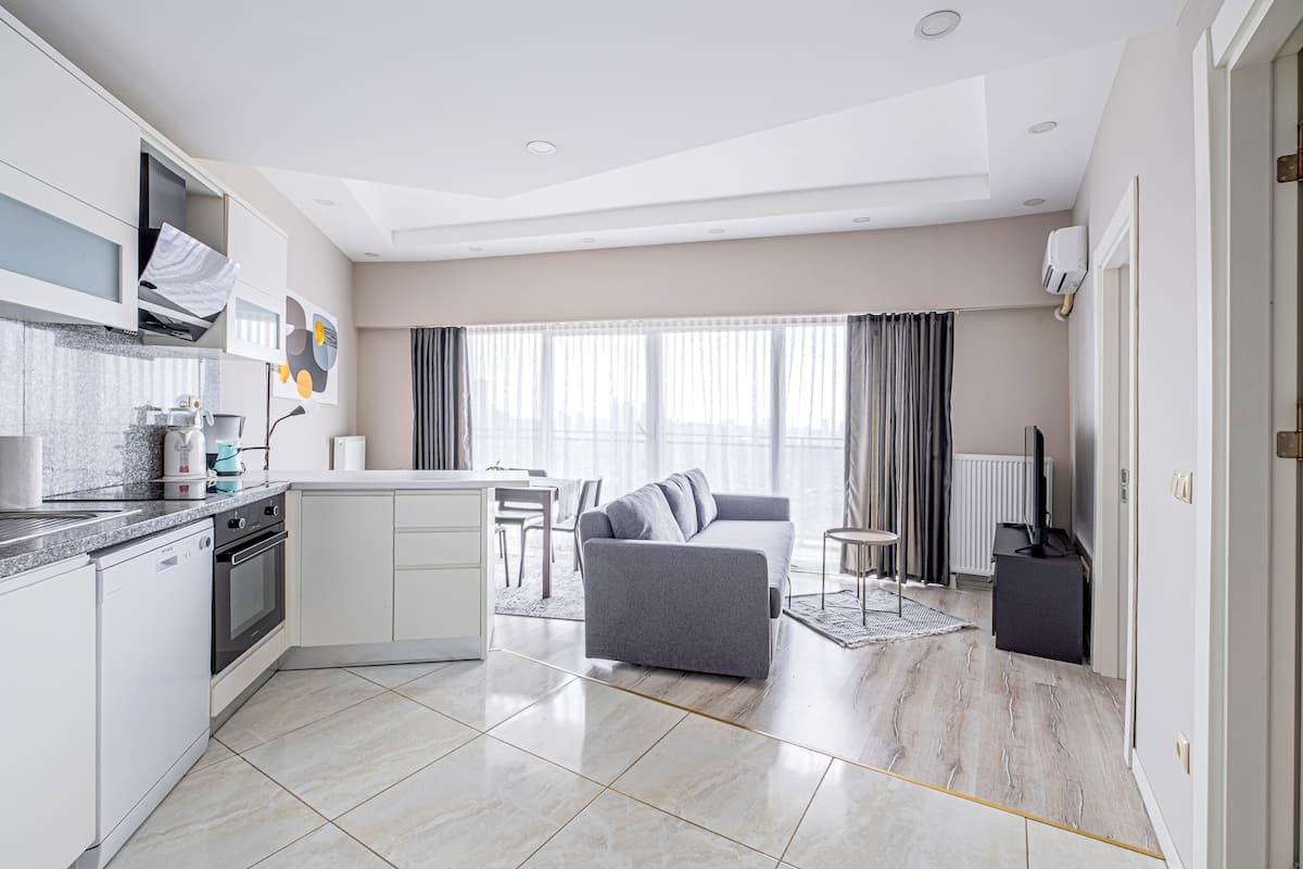 A modern kitchen with white cabinetry, a built-in oven, and a dining area with a gray sofa and a small round table.