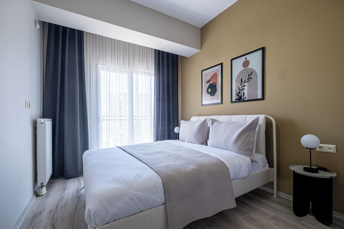 A modern bedroom with a bed, a bedside table, and a window with curtains.