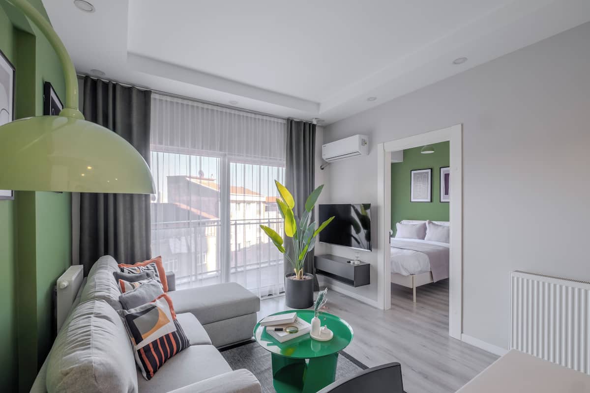 A modern living room with a sofa, a green coffee table, and a large window with curtains.