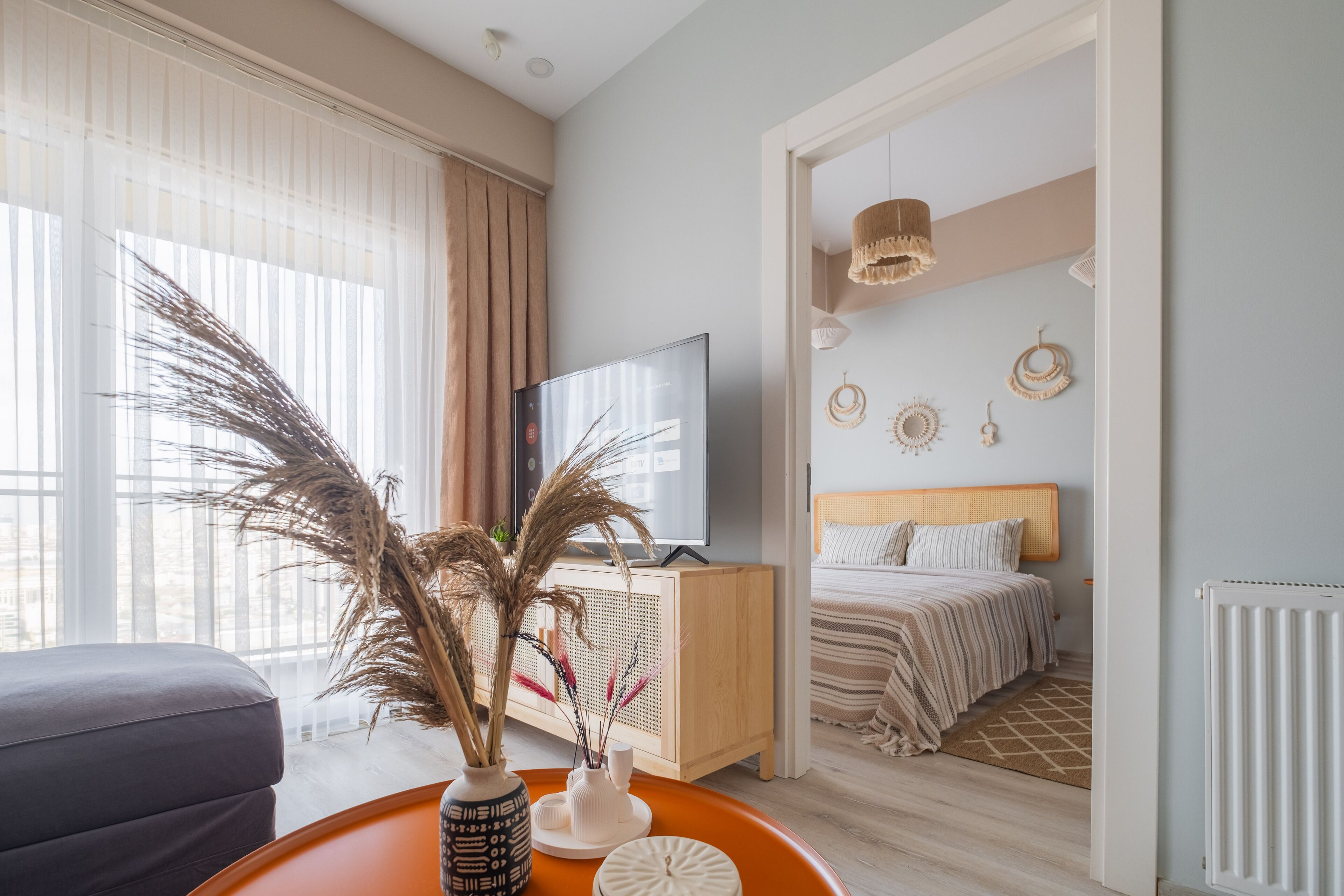 Ein modernes Hotelzimmer mit einem Bett, einem Fernseher, einer Holzkommode und einer Vase mit Trockenpflanzen.