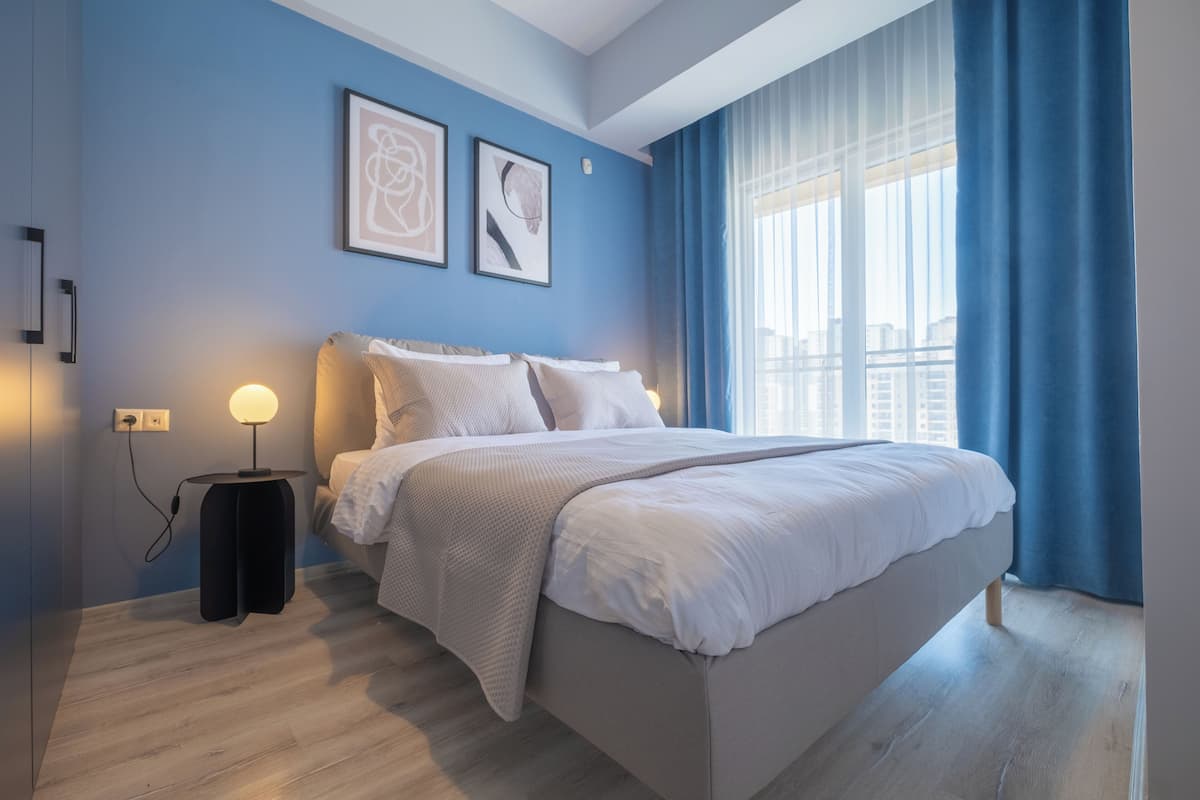 A modern bedroom with a large bed, a bedside table with a lamp, and artwork on the wall.