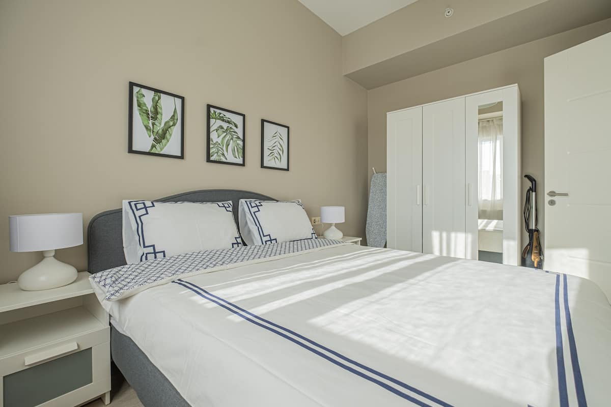 A neatly made bed with a white and blue striped bedspread, two bedside lamps, and three framed botanical prints on the wall.
