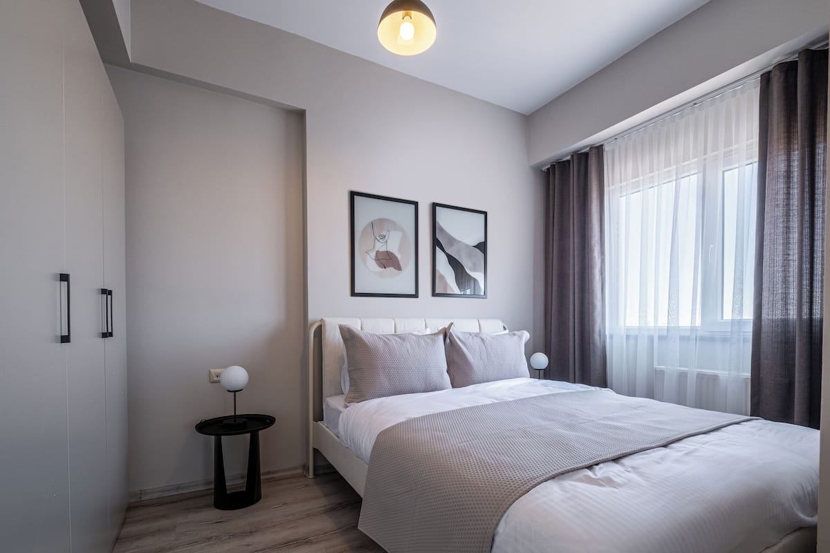A modern bedroom with a bed, a bedside table with a lamp, and two framed artworks on the wall.
