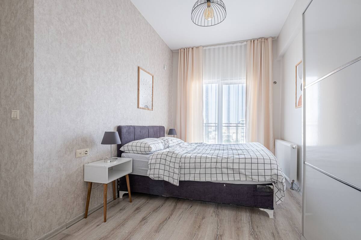 A modern bedroom with a bed, bedside tables, a radiator, and a window with curtains.