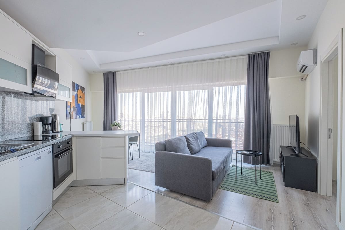 A modern kitchen with a built-in oven and a dining area with a gray sofa and a small table.