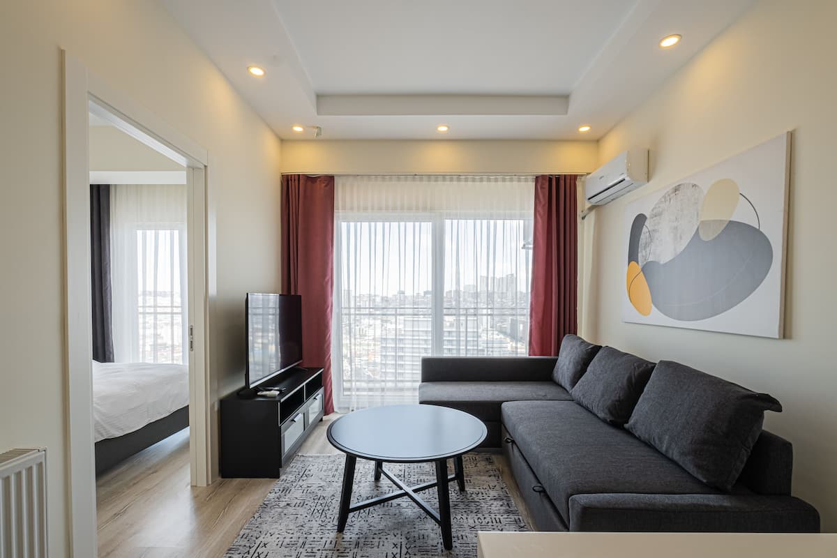 A modern living room with a sofa, a round coffee table, a TV, and a large window with curtains.