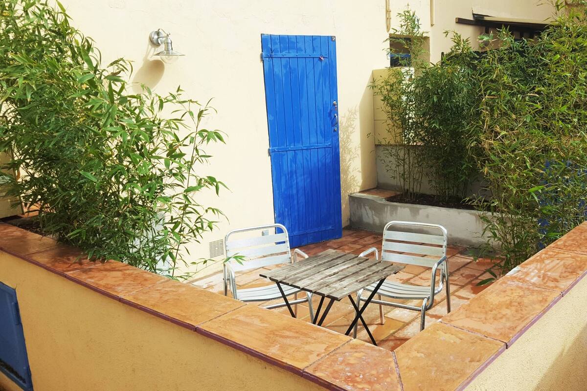 A patio with a table and chairs, a blue door, and potted plants.