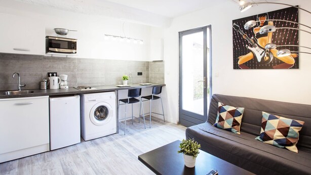 A modern kitchen with a microwave, sink, and washing machine. There is a dining area with a table and chairs, and a sofa with patterned cushions. A painting is on the wall. - GregBnb - Le Lacordaire - Toulon Ouest (Toulon)
