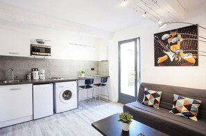 A modern kitchen with a microwave, sink, and washing machine. There is a dining area with a table and chairs, and a sofa with patterned cushions. A painting is on the wall. - GregBnb - Le Lacordaire - Toulon Ouest (Toulon)