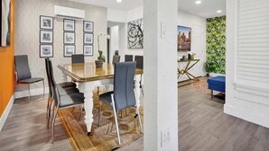 Ein moderner Essbereich mit einem Holztisch und Stühlen, gerahmten Bildern an der Wand und einem Stadtbildgemälde.