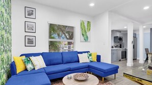 Ein modernes Wohnzimmer mit einem blauen Ecksofa, einem runden Couchtisch und einer Küche im Hintergrund.