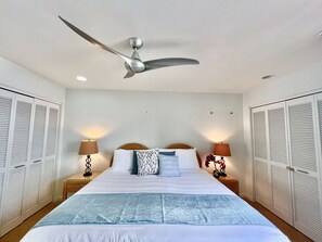 A bedroom with a bed, two bedside tables with lamps, a ceiling fan, and white louvered closets. - Island-Inspired 2bd with loft, lanais and serenity (Kihei)