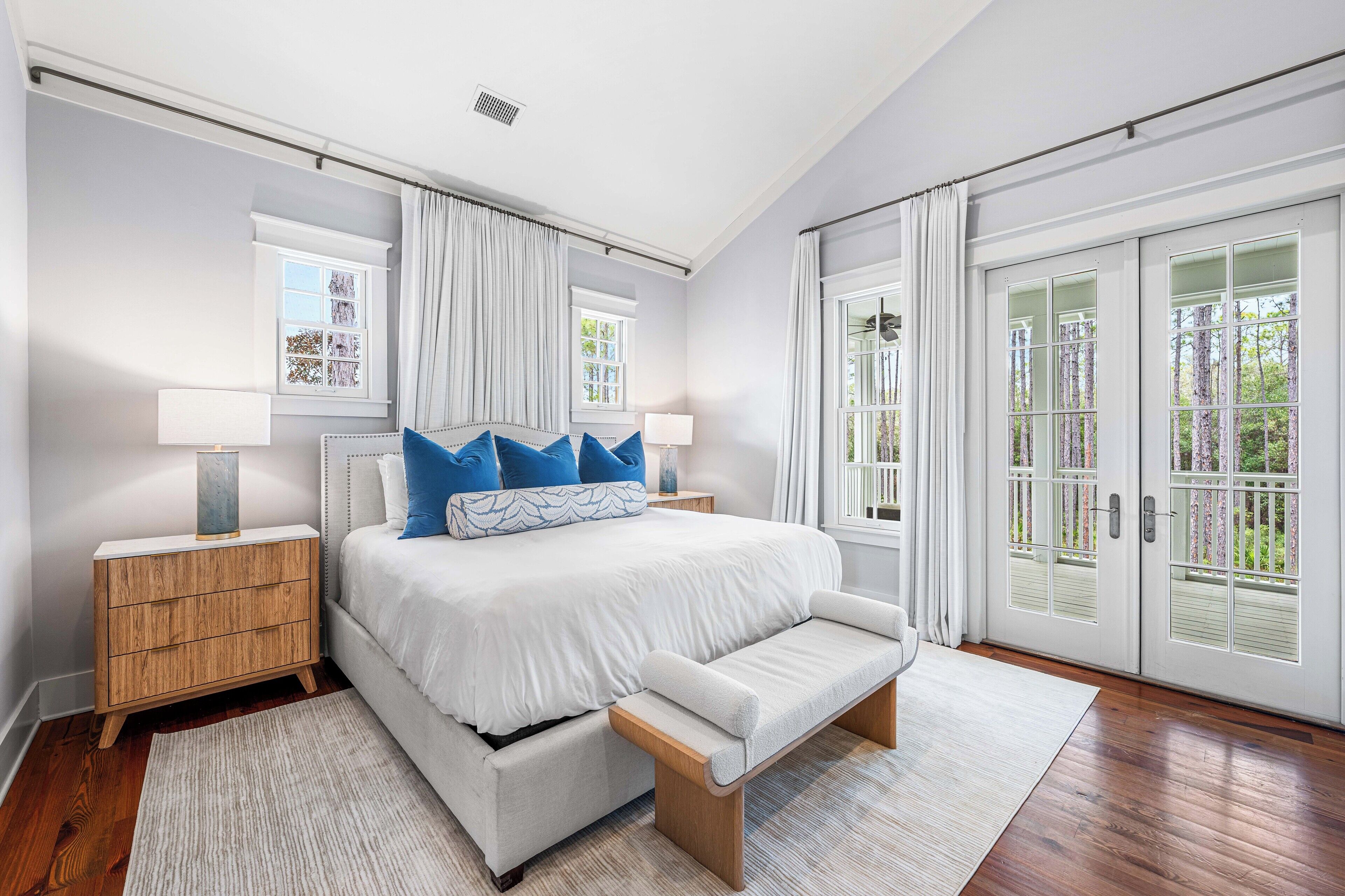 Un dormitorio con cama, mesitas de noche, un banco y vistas al exterior.