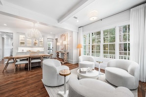 A spacious living room with a large window, a dining area with a wooden table, and modern furniture. - WaterColor Retreat: Private Pool, Golf Cart, Bikes, and Serene Luxury in WaterColor's Camp District! (Santa Rosa Beach)