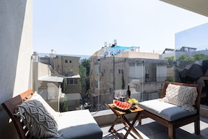 Enjoy a city view from this balcony with a bench, table, and comfortable seating.