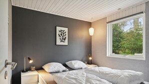 A bedroom with a bed, bedside tables, a wall-mounted light, and a window with a view of greenery. - 4 bedroom awesome home in Sæby (Sæby)