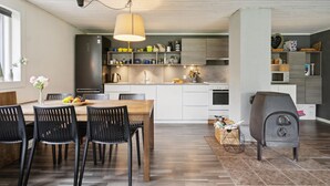 A modern kitchen with white cabinetry, a wooden dining table, black chairs, and a built-in stove. - 4 bedroom awesome home in Sæby (Sæby)