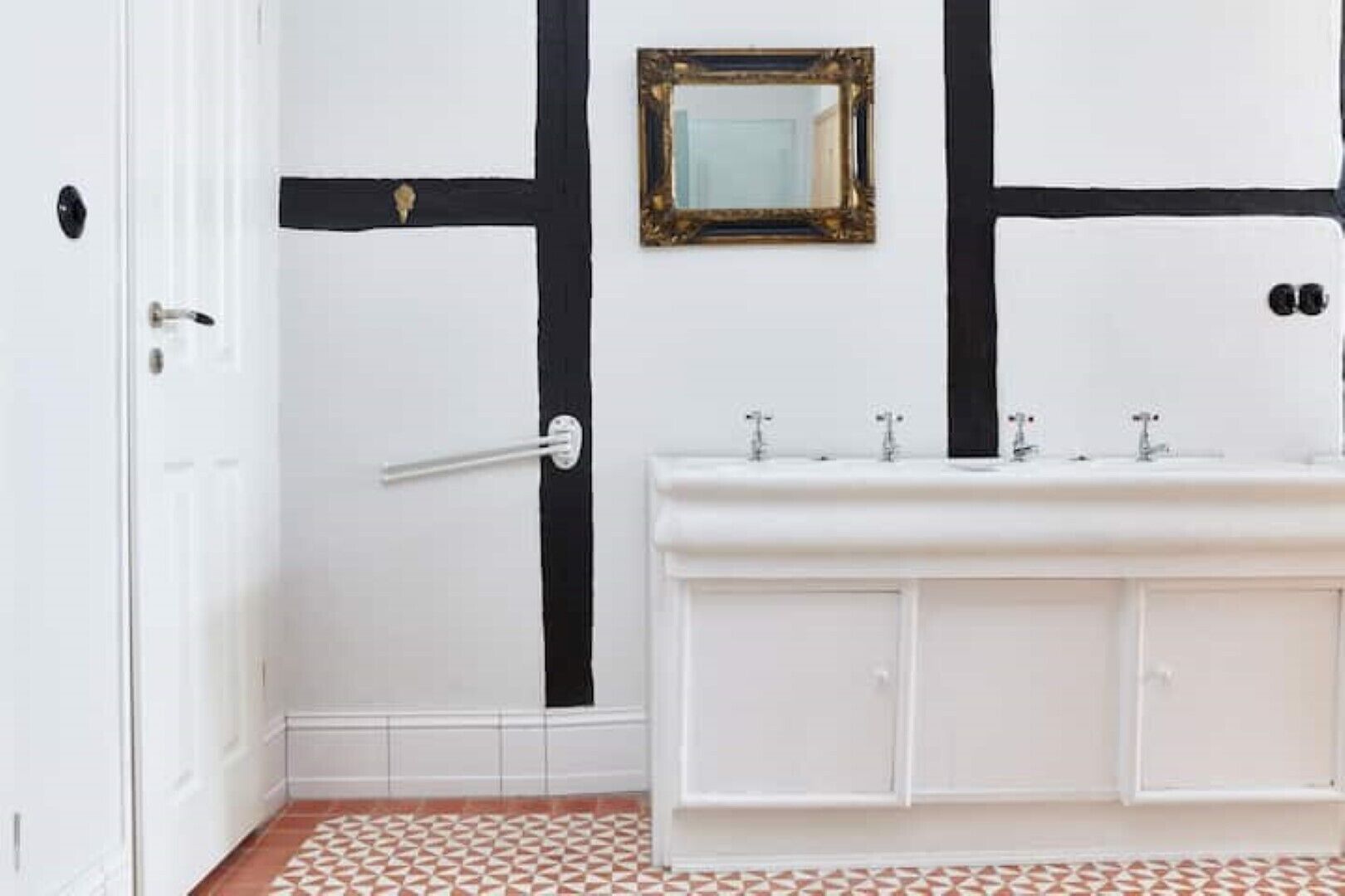 Um banheiro com toucador branco, detalhes em preto, um espelho e piso estampado.