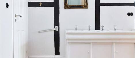 Um banheiro com toucador branco, detalhes em preto, um espelho e piso estampado.