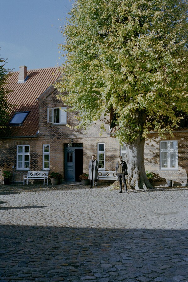 A traditional brick house with a cobblestone driveway, a bench, and a large tree in front. - Entire historic farmhouse with over 650 sqm & sea view (Fehmarn)