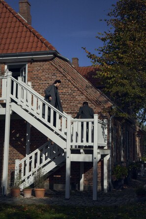 A person descending a white staircase outside a brick building with a red roof. - Entire historic farmhouse with over 650 sqm & sea view (Fehmarn)