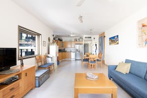 A modern living room with a TV, wooden furniture, a dining area, and a kitchen in the background.