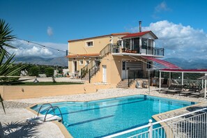 A pool area with a clear view of mountains, a two-story building with a balcony, and a covered seating area.