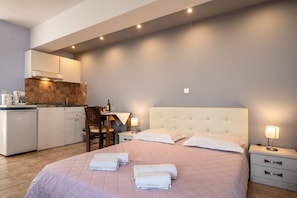 A bedroom with a large bed, bedside tables, a nightstand, a desk, and a kitchen area with cabinets and a coffee machine.