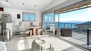 Eine moderne Küche mit Essbereich, eine große Schiebeglasdoor, die auf einen Balkon mit Blick auf das Meer und die Berge führt.