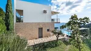 Ein modernes, zweistöckiges Gebäude mit Natursteinfassade, einem Balkon und einem Poolbereich.