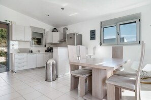 A modern kitchen with white cabinets, a stainless steel trash can, and a dining area with a wooden table and chairs. - Villa 'Villa Skorpios' with Sea View, Wi-Fi and Air Conditioning (Lefkadas)