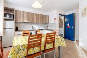 A kitchen with wooden cabinets, a microwave, a refrigerator, and a dining table with chairs. - Apartment 'Night and Day 4' with Mountain View, Balcony, and Wi-Fi (Predazzo)