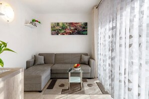 A modern living room with a grey sectional sofa, a small glass table with a vase, a painting on the wall, and a patterned rug. - Apartment 'Night and Day 4' with Mountain View, Balcony, and Wi-Fi (Predazzo)
