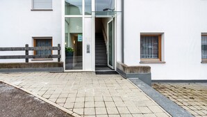A building entrance with a glass door, a staircase, and a small outdoor seating area.