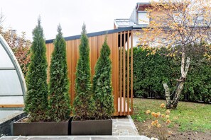 Un bâtiment moderne avec une façade en bois, un jardin planté de conifères et un ciel dégagé.