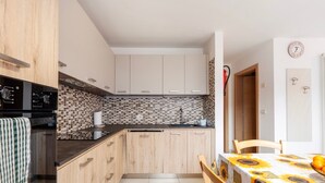 A compact kitchen with wooden cabinets, a tiled backsplash, and a dining area with a table set for two.