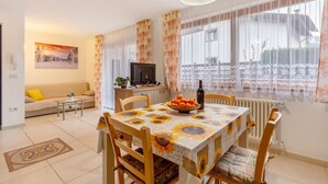 A dining area with a table set for four, a sofa, a TV, and a window with curtains.