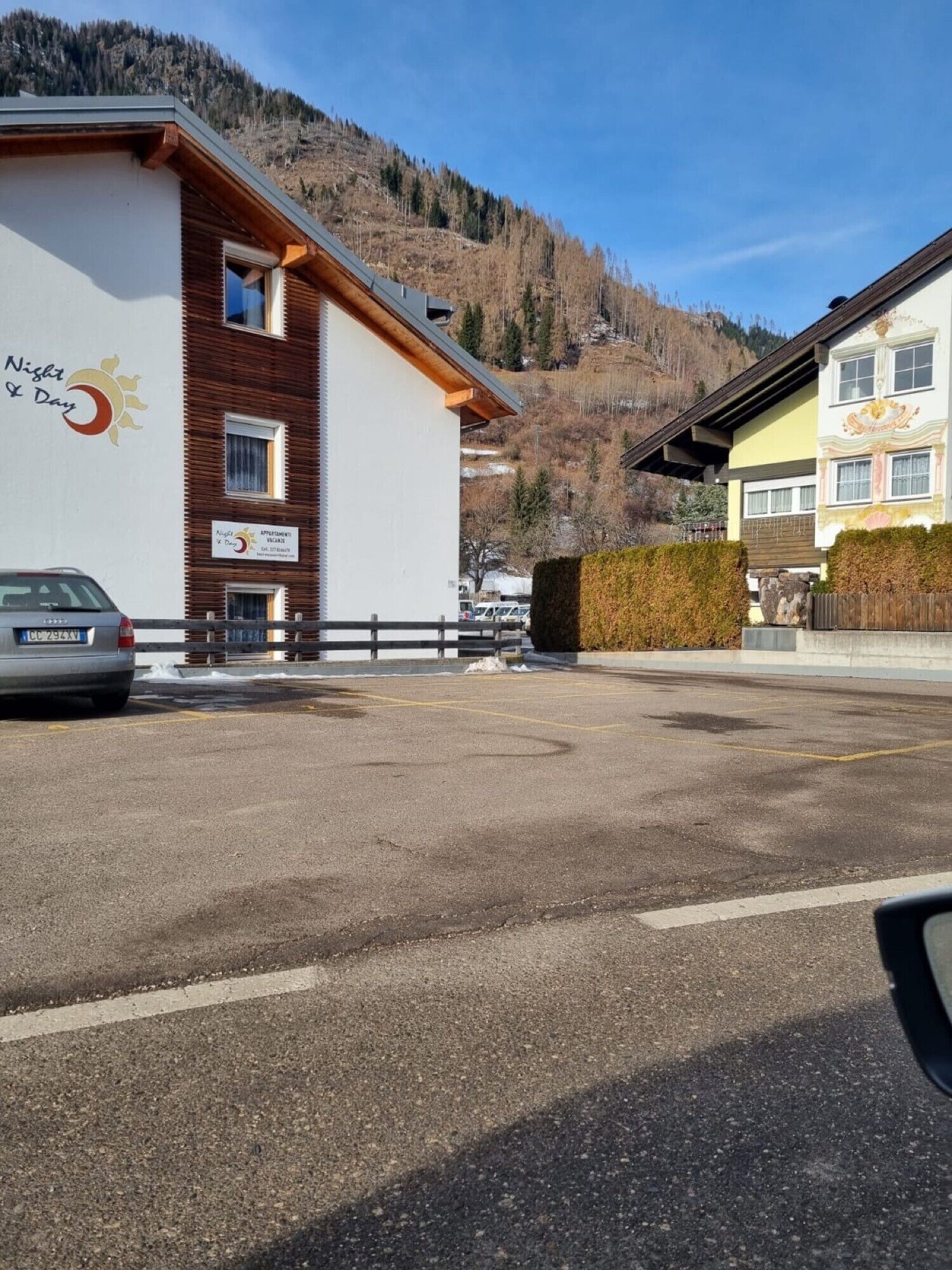 A hotel with a mountain backdrop, a parking lot, and a sign indicating 'Night & Day' accommodation.
