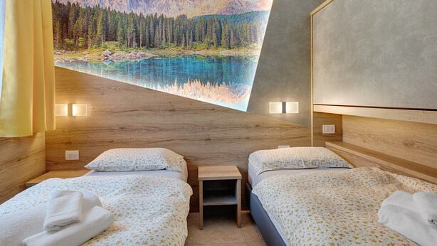 A hotel room with two beds, a small table, a painting of a mountain landscape, and a wooden headboard. - Apartment 'Night and Day 8' with Mountain View, Balcony and Wi-Fi (Predazzo)