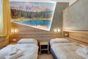 A hotel room with two beds, a small table, a painting of a mountain landscape, and a wooden headboard. - Apartment 'Night and Day 8' with Mountain View, Balcony and Wi-Fi (Predazzo)