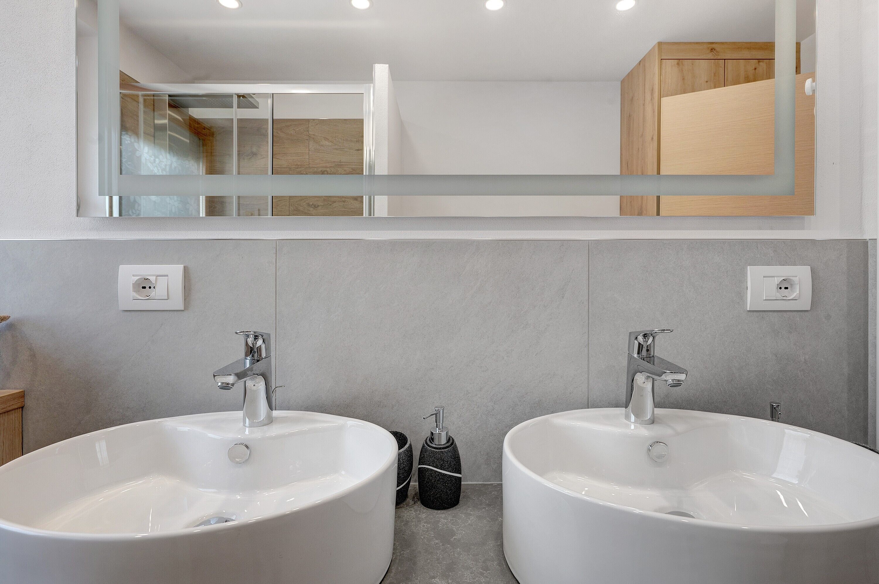 Une salle de bain avec deux lavabos blancs, un miroir et un meuble en bois.