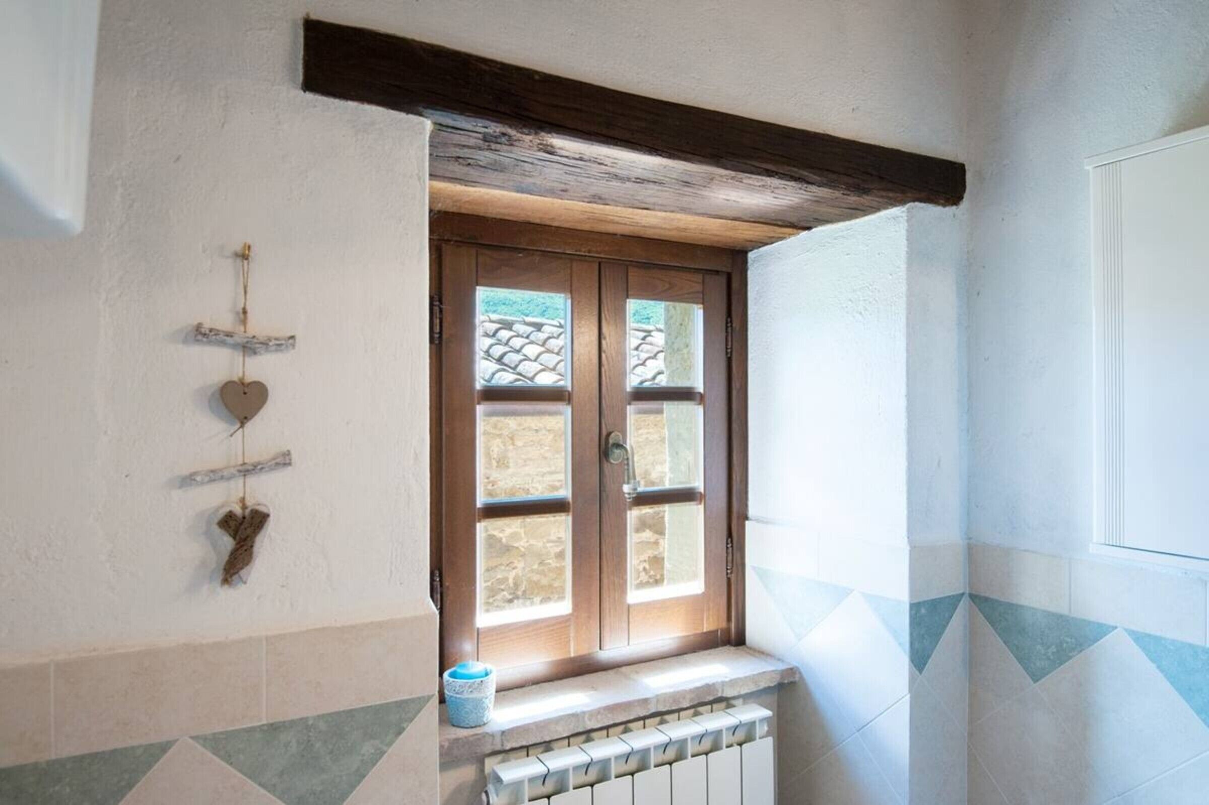 Ein Zimmer mit Fenster, Heizkörper und einer Wandablage mit einem herzförmigen Gegenstand.